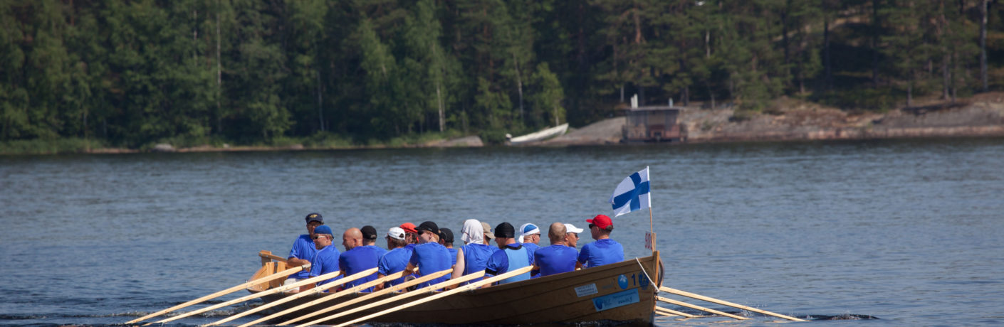 tyynellä järvellä kirkkovenesoutu ja veneen keulassa liehuu suomen lippu