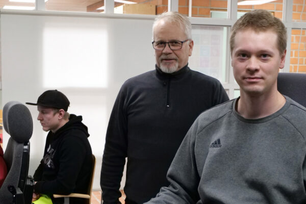 Heikki Kääriäinen istuu simulaattorin penkissä. Takana seisoo Asko Tolvanen. Taustalla näkyy opiskelijoita käyttämässä simulaattoria.