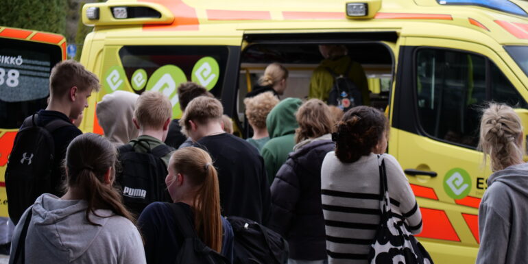 Kymmenkunta yläkoululaista tutustumassa Esedun perustason ensihoitajien koulutuskäytössä olevaan ambulanssiin ulkona.