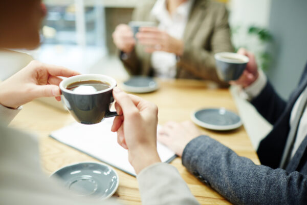 Cup of black tea or coffee held by businesswoman during coffee-break with colleagues