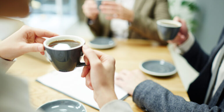 Cup of black tea or coffee held by businesswoman during coffee-break with colleagues