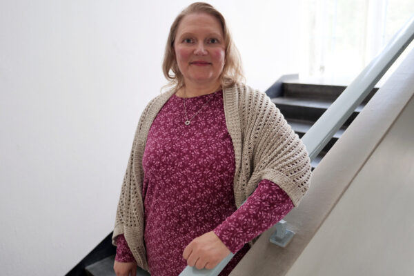 Nainen nojaa portaikossa kaiteeseen ja katsoo hymyillen kameraan