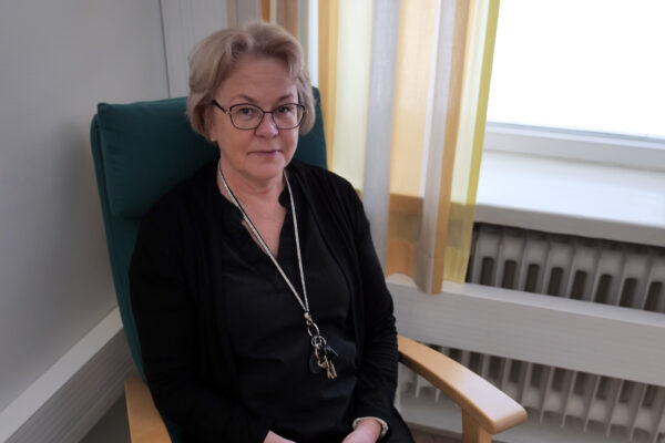 Nainen istuu nojatuolissa ja katsoo hymyillen kameraan