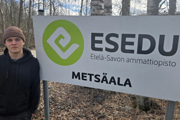 Nuori mies nojaa kylttiin, jossa lukee Etelä-Savon ammattiopisto metsäala