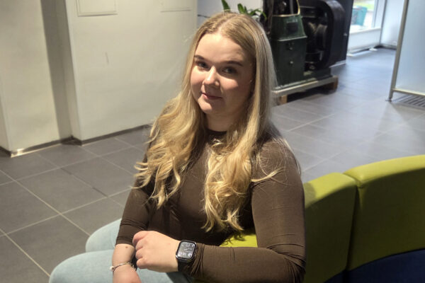 Nainen istuu sohvalla katsoen kameraan
