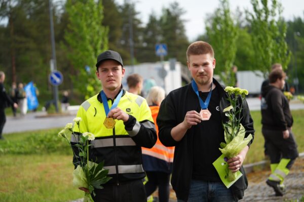 Kaksi miestä katsoo kameraan ja pitää käsissään kaulalla roikkuvia mitaleja