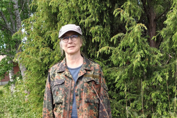 Nainen seisoo vihreän puun edessä katsoen kameraan